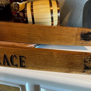 Op de afbeelding: Twee houten duigen met de woorden "Rare" en "Trace" in zwart ge&euml;tst. De duigen zijn lichtbruin van kleur met donkere verkoolde uiteinden. Een klein houten vat en flessen drank staan op de achtergrond.