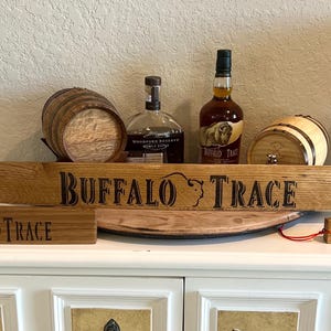 Puede incluir: Una exhibici&oacute;n con art&iacute;culos tem&aacute;ticos de bourbon Buffalo Trace. Incluye un letrero de madera con el nombre de la marca, un barril peque&ntilde;o, botellas de bourbon y una peque&ntilde;a etiqueta de madera que dice "Bourbon".