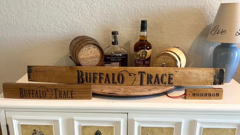 Puede incluir: Una exhibici&oacute;n con art&iacute;culos tem&aacute;ticos de bourbon Buffalo Trace. Incluye un letrero de madera con el nombre de la marca, un barril peque&ntilde;o, botellas de bourbon y una peque&ntilde;a etiqueta de madera que dice "Bourbon".