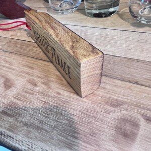 May include: A wooden bottle stopper with the text "BUFFALO TRACE" engraved on the side. The stopper is rectangular and made of light brown wood. A red string is attached to the stopper. Several glasses are in the background.