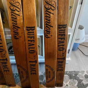 May include: Several wooden planks with the words "Blanton's" and "BUFFALO TRACE" printed in black. The planks are made of a light brown wood and appear to be from a barrel. The text "SOUR MASH BOURBON WHISKEY" is also printed on the planks.