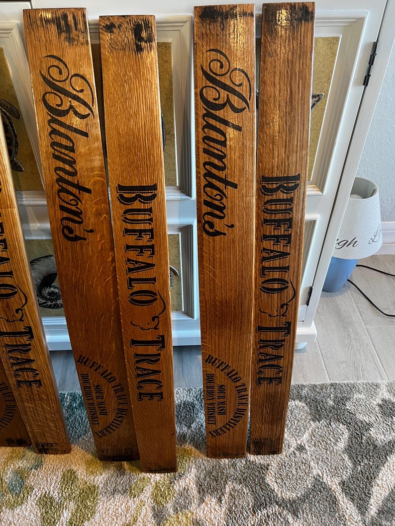May include: Several wooden planks with the words "Blanton's" and "BUFFALO TRACE" printed in black. The planks are made of a light brown wood and appear to be from a barrel. The text "SOUR MASH BOURBON WHISKEY" is also printed on the planks.
