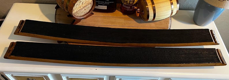 Op de afbeelding: Twee gebogen, rechthoekige houten trays met donkere, getextureerde centra en lichtbruine randen. De trays zijn gemaakt van gerecyclede vatenstaven, die de natuurlijke houtnerf laten zien. De trays worden gepresenteerd op een wit oppervlak.