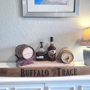 May include: A display featuring a wooden barrel, bottles of liquor, and a lamp with a lampshade that says "Laugh Love". The display sits on a wooden plank with the words "Buffalo Trace" on it.