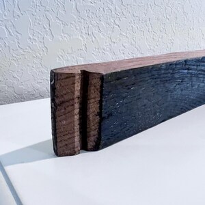 May include: A rectangular piece of wood with a dark blue-black finish on one side and a natural brown finish on the other. The end of the wood has a carved design with two vertical grooves. The wood is likely for home decor.