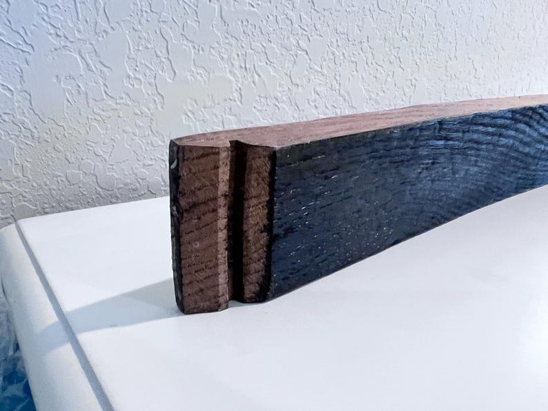 May include: A rectangular piece of wood with a dark blue-black finish on one side and a natural brown finish on the other. The end of the wood has a carved design with two vertical grooves. The wood is likely for home decor.