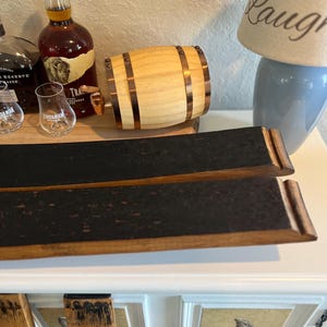 May include: A wooden barrel-shaped dispenser with copper-colored bands and a spigot. Two curved, charred wood pieces are in the foreground. A bottle of liquor and two glasses are on a wooden tray. A lamp with the word "Laugh" is in the background.