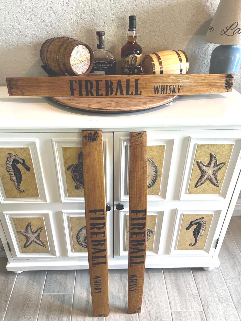Puede incluir: Letrero de madera con el texto "FIREBALL WHISKY" en letras negras. El letrero est&aacute; hecho de madera de color marr&oacute;n claro y se muestra con dos piezas verticales a juego. El fondo incluye botellas de whisky y un mueble decorativo.