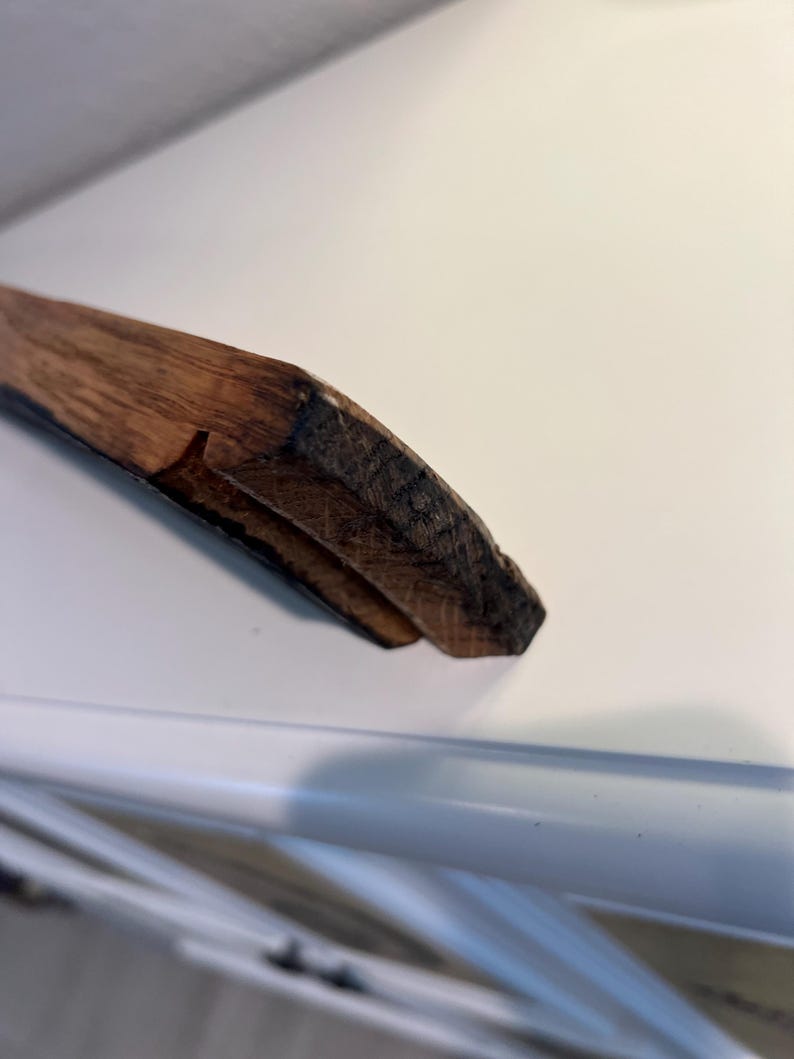 May include: Close-up of a wooden object with a dark brown, textured surface. The object appears to be a piece of a larger structure, possibly a frame or a decorative element. The wood grain is visible, and the edges are rough.