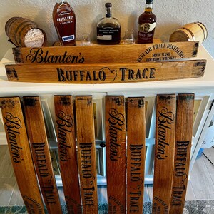 May include: A display of bourbon bottles and barrel stave signs. The signs are made of wood and feature the names "Blanton's" and "Buffalo Trace" in black lettering. The bottles are various shapes and sizes, with labels visible. Small wooden barrels are also present.