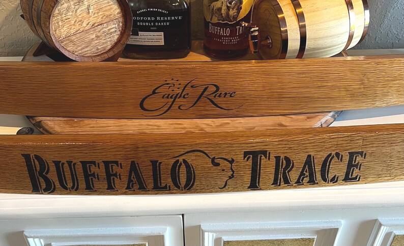 Op de afbeelding: Houten duigen met de tekst "Eagle Rare" en "Buffalo Trace" in zwart. De duigen worden weergegeven voor drankflessen en kleine houten vaten, wat wijst op een thema van whisky of bourbon.
