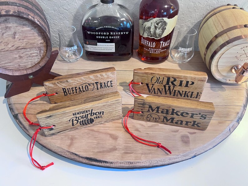 May include: Wooden bourbon barrel stave tags with the names "Buffalo Trace", "Kentucky Bourbon Trail", "Old Rip Van Winkle", and "Maker's Mark" printed on them. Each tag has a red string attached.