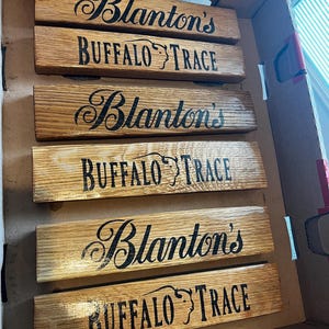 Puede incluir: Seis tablones de madera con las palabras "Blanton's" y "Buffalo Trace" estampadas en negro. Los tablones est&aacute;n colocados dentro de una caja de cart&oacute;n. La madera tiene una veta natural y un tono marr&oacute;n c&aacute;lido.