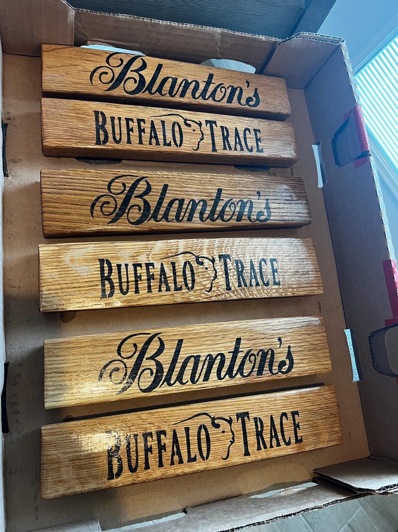 Puede incluir: Seis tablones de madera con las palabras "Blanton's" y "Buffalo Trace" estampadas en negro. Los tablones est&aacute;n colocados dentro de una caja de cart&oacute;n. La madera tiene una veta natural y un tono marr&oacute;n c&aacute;lido.