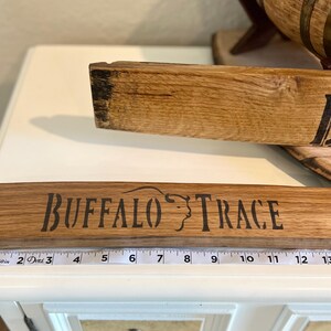 Puede incluir: Dos tablas de madera con las palabras "BUFFALO TRACE" y "BU" en letras negras. La tabla inferior mide aproximadamente 35,5 cm de largo. La madera tiene una veta natural y es de color marr&oacute;n claro.