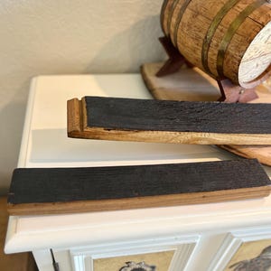 Puede incluir: Dos duelas de barril de madera recuperada con una superficie oscura y carbonizada y bordes de madera natural. Las duelas son rectangulares y parecen provenir de una barrica de whisky. Un peque&ntilde;o barril de madera es visible en el fondo.