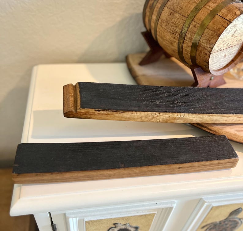 Puede incluir: Dos duelas de barril de madera recuperada con una superficie oscura y carbonizada y bordes de madera natural. Las duelas son rectangulares y parecen provenir de una barrica de whisky. Un peque&ntilde;o barril de madera es visible en el fondo.