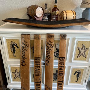 May include: A white cabinet with decorative seahorse and starfish panels, topped with a wooden barrel stave and various bottles and miniature barrels. Four wooden barrel staves with "Blanton's" and "Buffalo Trace" text are in front.