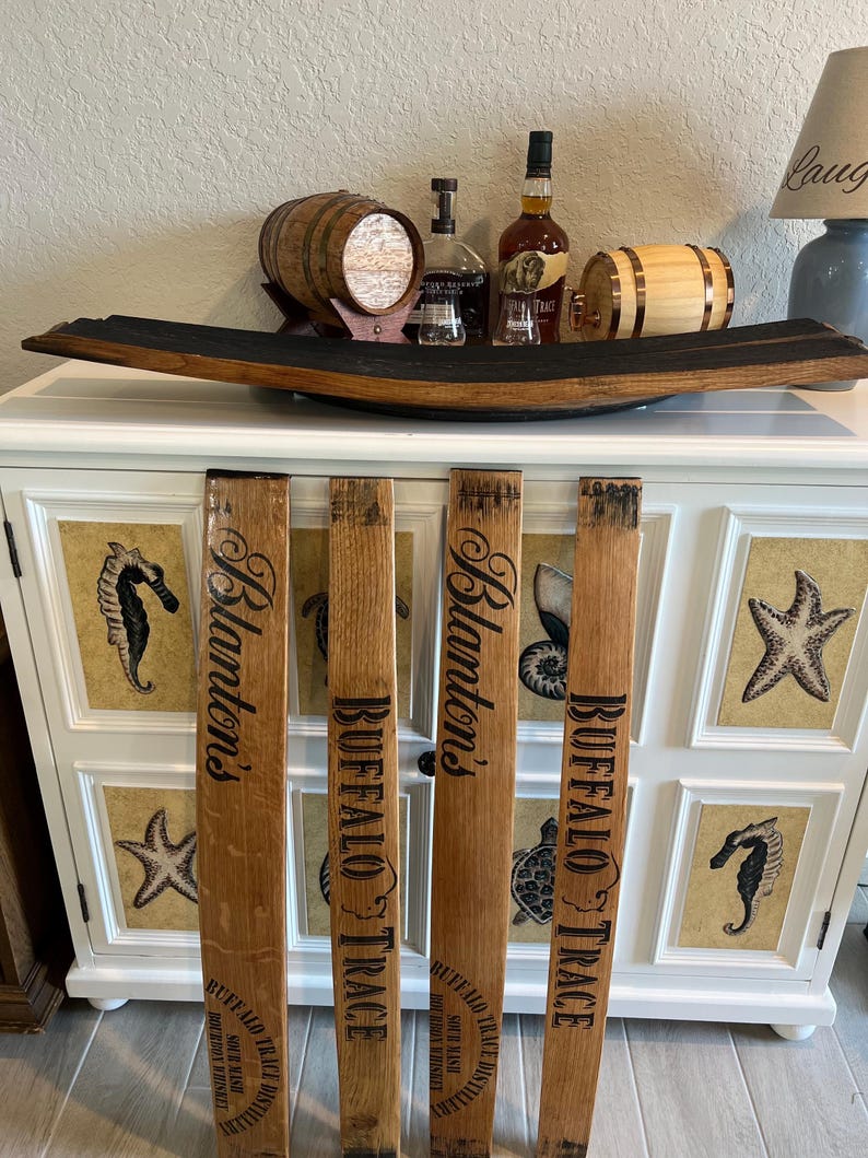 May include: A white cabinet with decorative seahorse and starfish panels, topped with a wooden barrel stave and various bottles and miniature barrels. Four wooden barrel staves with "Blanton's" and "Buffalo Trace" text are in front.