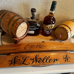 May include: A collection of bourbon-related items, including two small wooden barrels, two bottles of bourbon, and two wooden barrel staves. The staves are engraved with the names "Eagle Rare" and "W.L. Weller".