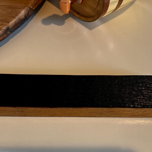 Puede incluir: Un objeto rectangular de madera con una parte superior te&ntilde;ida de negro oscuro y una base de color madera natural. El art&iacute;culo parece ser una peque&ntilde;a estanter&iacute;a o pieza de exhibici&oacute;n, mostrando un contraste entre los tonos de madera oscuros y claros.