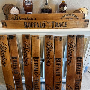 May include: Wooden barrel stave decor with the words "Blanton's" and "Buffalo Trace" in black lettering. The image also shows bottles of bourbon and small wooden barrels. The wood has a natural, aged appearance.
