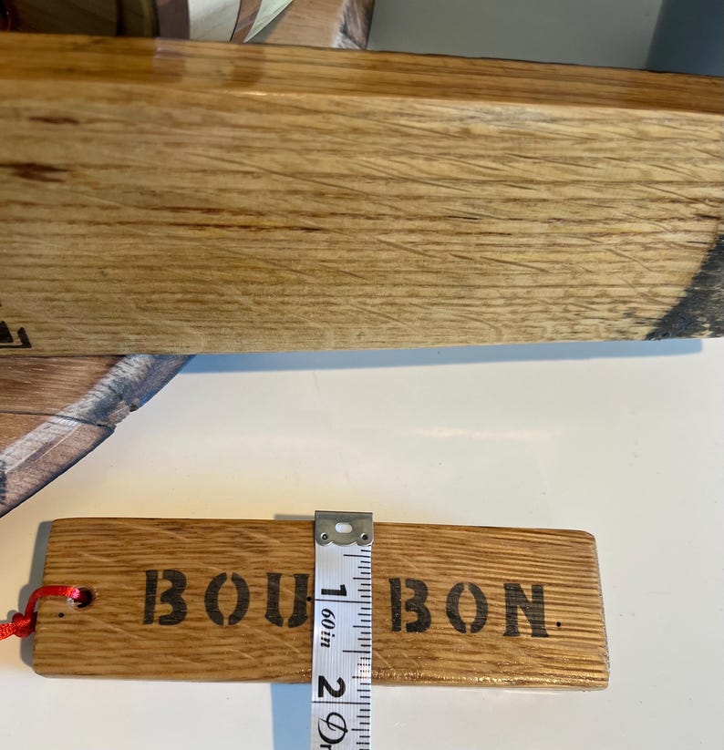 Puede incluir: Una etiqueta rectangular de madera con la palabra "BOURBON" impresa en negro. La etiqueta mide aproximadamente 2,5 cm de ancho. Una cuerda roja est&aacute; adjunta. La etiqueta es de madera marr&oacute;n claro.