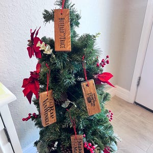 May include: A small artificial Christmas tree decorated with wooden ornaments. The ornaments are rectangular and feature the names "Buffalo Trace", "Old Rip Van Winkle", "Kentucky Bourbon", and "Maker's Mark". Red berries and poinsettias add color.