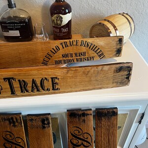 May include: Wooden bourbon barrel stave signs with the text "Buffalo Trace Distillery" and "Trace" in black lettering. Two bottles of bourbon and a small barrel are also visible. The signs are made from reclaimed wood.
