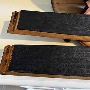 Op de afbeelding: Twee rechthoekige houten serveerplanken. De planken hebben een donker, getextureerd oppervlak dat wordt omlijst door lichter gekleurd hout. De uiteinden van de planken hebben een decoratief, gekerfd ontwerp. De planken zijn waarschijnlijk bedoeld om voedsel te serveren.