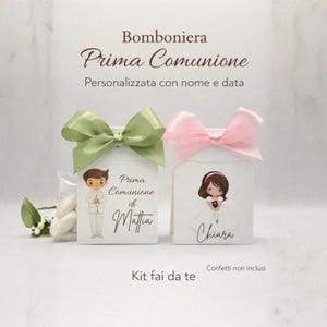 Puede incluir: Dos cajas de recuerdos blancas con ilustraciones de niños, atadas con lazos verdes y rosas. El texto en las cajas dice "Prima Comunione" y nombres personalizados. La imagen también incluye el texto "Kit fai da te".