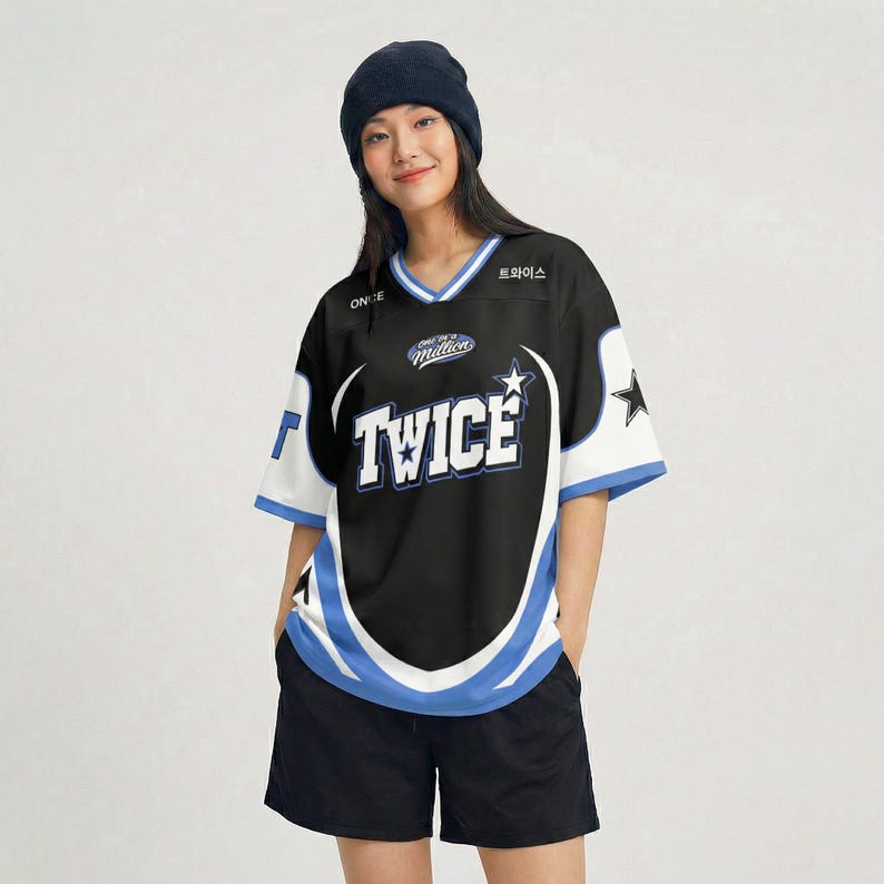 Puede incluir: Camiseta negra y blanca con la palabra "TWICE" en letras blancas grandes. La camiseta tiene detalles azules y blancos, cuello en V y un gr&aacute;fico de estrella. La persona de la imagen lleva un gorro azul marino y pantalones cortos negros.