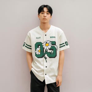 May include: Cream-colored baseball jersey with the word "ILLIT" above the chest and "SEOUL" above the right chest. The jersey features a large green "05" with daisy flowers and green stripes on the sleeves.