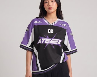 May include: A black, white, and purple jersey-style shirt with the word "ATEEZ" and the number "08" printed on the front. The shirt has a V-neck and short sleeves. The model is wearing a black pleated skirt.