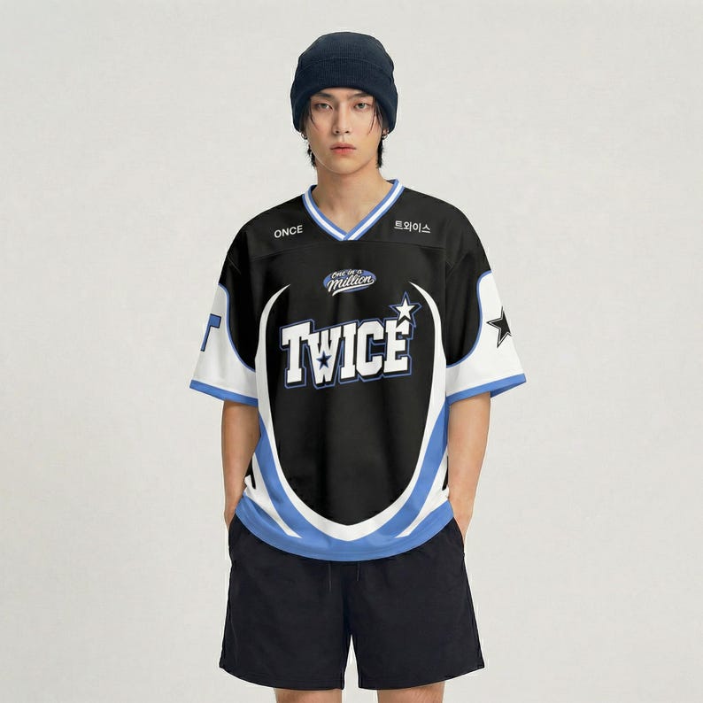 Puede incluir: Camiseta de estilo jersey en blanco y negro con la palabra "TWICE" en letras blancas grandes. La camiseta tiene detalles en azul y blanco, cuello en V y mangas cortas. La palabra "ONCE" est&aacute; impresa en la parte superior izquierda y texto coreano en la parte superior derecha.