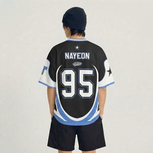 Puede incluir: Camiseta negra y blanca con el nombre "NAYEON" y el n&uacute;mero "95" en la espalda. La camiseta tiene detalles en azul y blanco y un gr&aacute;fico de estrella. La persona lleva un gorro negro y pantalones cortos negros.