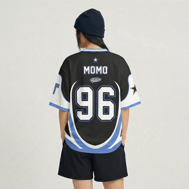 Puede incluir: Camiseta negra estilo jersey con detalles en blanco y azul, con el nombre "MOMO" y el n&uacute;mero "96" en blanco. La camiseta tiene mangas cortas y cuello redondo. Un gorro negro y pantalones cortos negros completan el look.