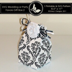 May include: A white gift box with a black damask pattern, topped with a white flower and black and white ribbons. The box is labeled "SVG Wedding or Party Favors Gift Box 2" and is 8.5" x 11".