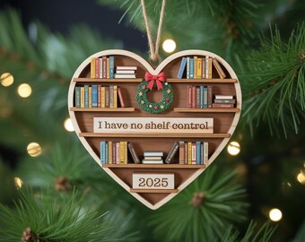 May include: Heart-shaped wooden Christmas ornament with a bookshelf design. The ornament features miniature books, a small wreath, a red bow, and the text "I have no shelf control" and the year "2025".