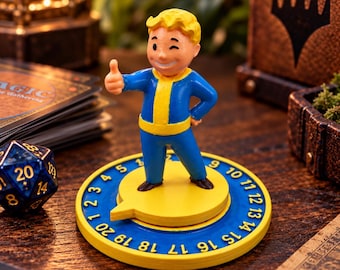 Puede incluir: Una figura de Vault Boy con cabello amarillo y un traje azul y amarillo, haciendo un gesto de pulgar hacia arriba. La figura se apoya sobre un contador circular amarillo y azul marcado con números del 1 al 20 para juegos de mesa.