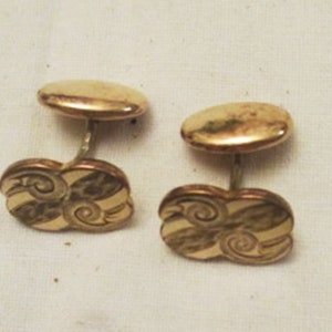 May include: A pair of vintage gold-toned cufflinks. Each cufflink features an oval top connected to a decorative base with a swirling, striped design. The cufflinks are set against a neutral background.