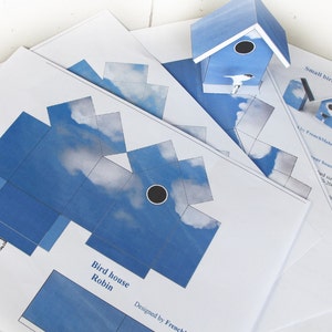 May include: Printable papercraft template for a birdhouse shaped like a robin. The template features a blue and white sky design with clouds. The text "Bird house Robin" and "Designed by French Melody" are included on the template.