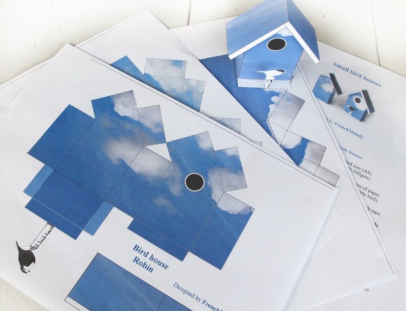 May include: Printable papercraft template for a birdhouse shaped like a robin. The template features a blue and white sky design with clouds. The text "Bird house Robin" and "Designed by French Melody" are included on the template.
