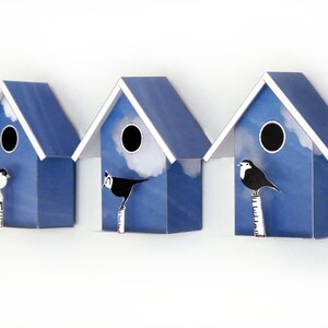 May include: Three blue birdhouses with white trim and a white cloud design. Each birdhouse has a round opening and a small bird perched on a branch in front of it.