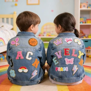 Puede incluir: Dos chaquetas vaqueras infantiles con parches coloridos. Una chaqueta tiene el nombre "AC" y la otra dice "EVELY". Los parches incluyen una pelota de baloncesto, un arcoíris, un rayo y una mariposa.