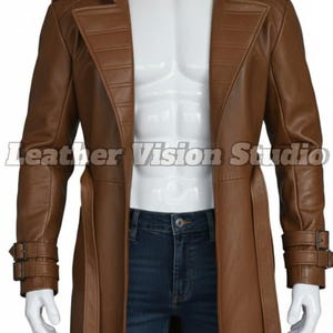 May include: A brown leather trench coat with a wide collar, belt, and buckle details. The coat is displayed on a mannequin with blue jeans. The Leather Vision Studio logo is visible.