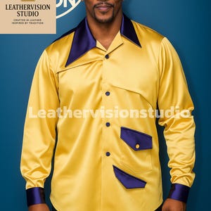Può includere: Una camicia di raso gialla con dettagli blu navy sul colletto, sui polsini e sulle tasche. La camicia a maniche lunghe ha una chiusura con bottoni. Il testo "LeatherVision Studio" è visibile sulla camicia.