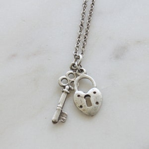 Op de afbeelding: Een zilveren ketting met een hartvormig hangslot en een sleutelbedel.