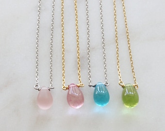 May include: Five delicate necklaces with different colored gemstone pendants. The necklaces are on a white background. The pendants are teardrop shaped and are in shades of pink, blue, and green.