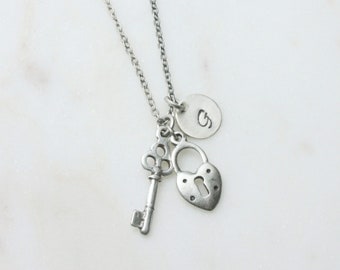 May include: A silver necklace with a heart-shaped padlock, a key, and a circular charm with the letter "S" engraved on it.